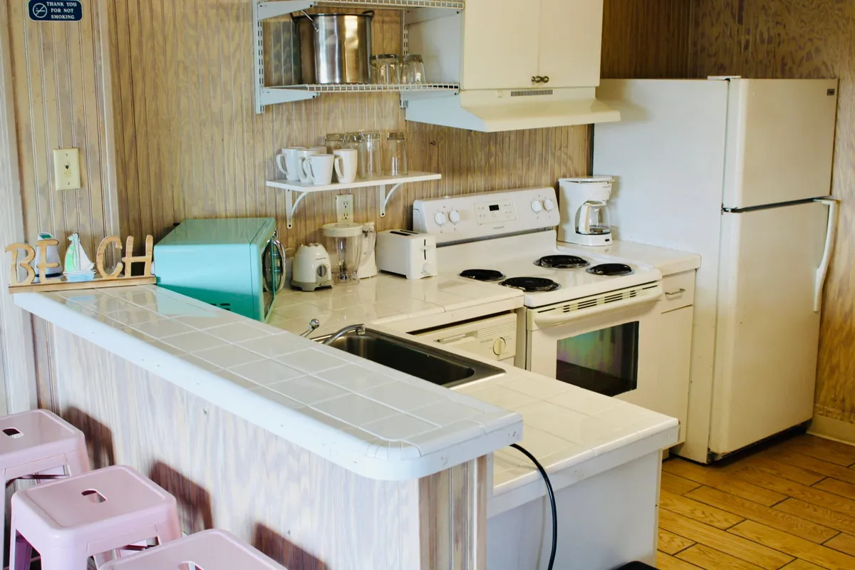 A cozy kitchen area decorated with beach-themed accents, featuring modern appliances, countertop seating, and ample space for socializing or enjoying a meal. The open layout allows natural light to flow through, complementing the studio's bright, welcoming feel.