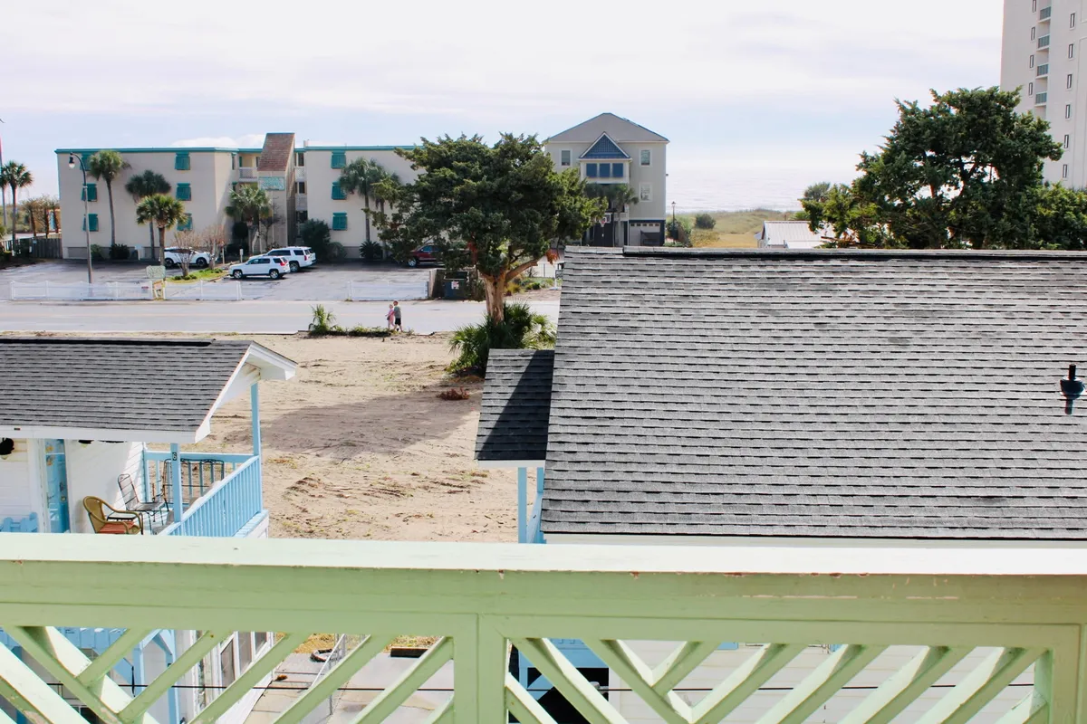 This image captures a cheerful, open scene featuring beachside houses with diverse architectural styles, swaying palm trees, and an inviting view toward the distant golden beach. The open spaces and balconies suggest opportunities for socializing, relaxing outdoors, and easy access to both the sand and nearby activities.