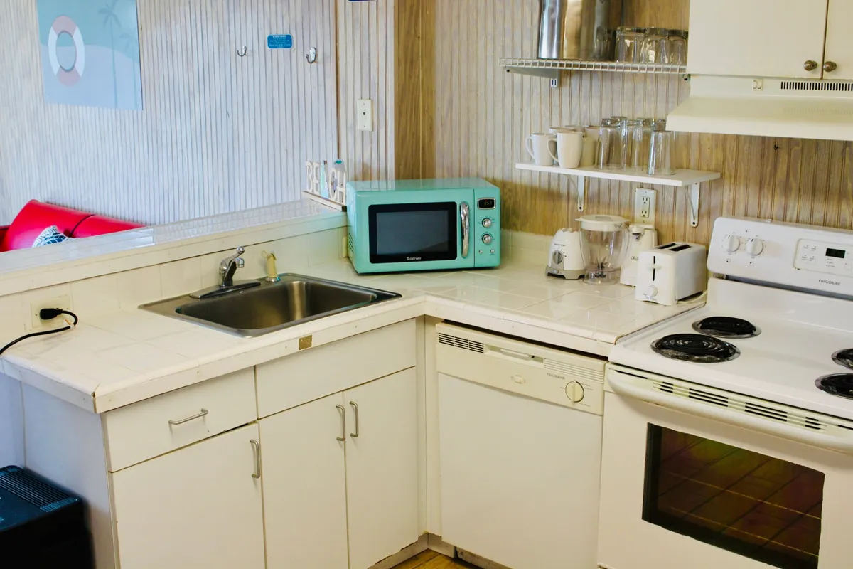 A compact kitchenette featuring a kitchen sink, microwave, stove, and toaster. The workspace is well-organized with clean countertops, appliances arranged for convenience, and a cheerful, homey atmosphere that invites cooking and social gatherings. The image clearly showcases the key amenities mentioned in the section, including the stove and microwave, and hints at the practical layout for preparing meals and snacks.